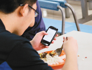 8日在西安一高校食堂内,一名大学生边吃饭边看手机